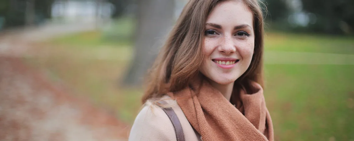 Mulher com roupas de inverno e no fundo um parque.